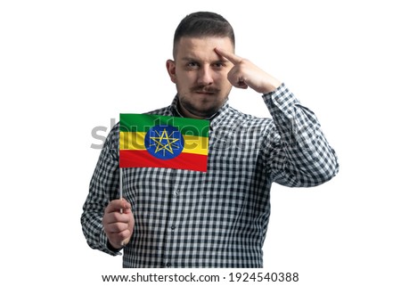 White guy holding a flag of Ethiopia and a finger touches the temple on the head isolated on a white background.