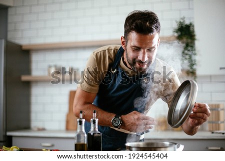 Handsome man preparing pasta in the kitchen. Guy cooking a tasty meal. Royalty-Free Stock Photo #1924545404