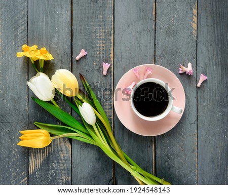A coffee cup with yellow tulips on wooden background. Flat lay, top view. Concept of holiday, birthday, Easter, valentines day