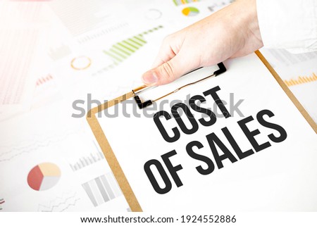 Text COST OF SALES on white paper plate in businessman hands with financial diagram. Business concept