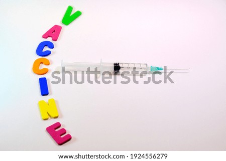 Syringe on a white background and with the word vaccine with colored letters.
