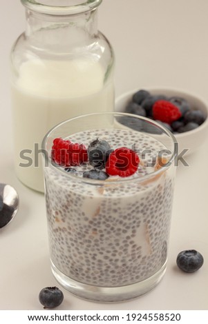 Chia seed pudding with blueberries, raspberries and pieces of mango, bowl of fresh berries and a bottle of milk on white background.  Gluten-free keto superfood concept. Copy space, stock photo