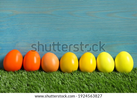 Easter eggs on green grass against light blue wooden background