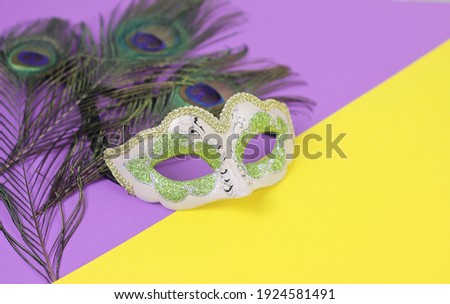 Beautiful carnival or Mardi Gras venice mask on peacock feathers background.Holiday decorations on bright purple and yellow backdrop.