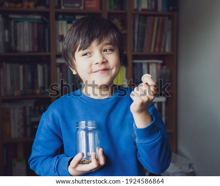 Low key light portrait of Happy Young Kid holding money coins in clear jar,  Smiling Child counting his saved coins, Cute boy holding coin, Children learning about saving for future concept Royalty-Free Stock Photo #1924586864