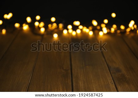 Blurred view of beautiful glowing lights, focus on wooden table. Space for text