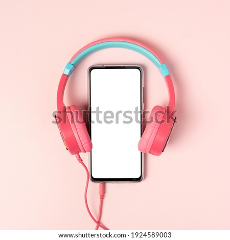 A top view on the smartphone with white screen and earphones on pink background. Studio shot concept about communication and music. Mock up template, flat lay, copy space. Royalty-Free Stock Photo #1924589003