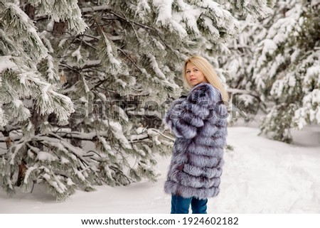 Young blonde woman in a fluffy fur coat for a walk in the fir forest
