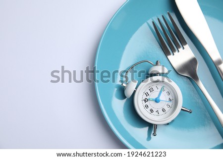 Alarm clock, plate and cutlery on white background, top view. Diet regime Royalty-Free Stock Photo #1924621223