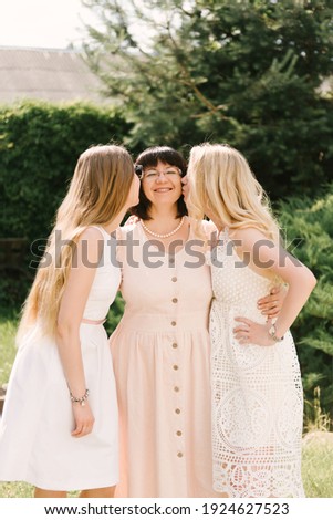 happy family outdoors on the grass in a park. mom and two adult daughters kiss her