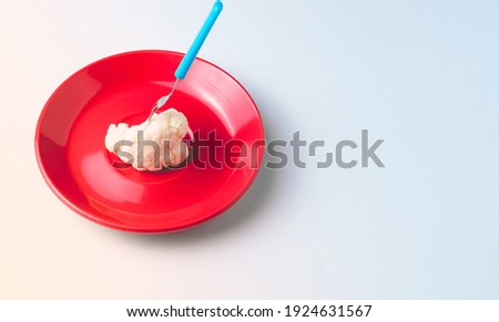 Piece of pricked cauliflower with a small blue fork on a red plate on a white background.