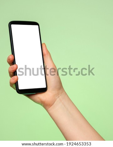 Smartphone upright with a blank screen in a woman's hand on a green background.