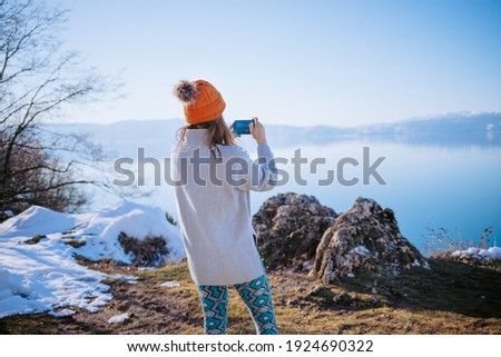 Young woman taking photos of lake in winter