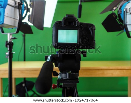 Filming set up with a camera, lights and a green screen 
