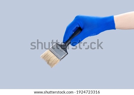 handyman repair minimal concept. worker holding paint brush isolated over gray background.