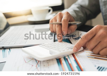 Asian male finance staff is calculating by using a calculator. Investment results to report to his boss at the meeting. On the table in the office, the concept of calculating investment results Royalty-Free Stock Photo #1924731596