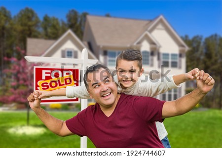 Hispanic Father and Mixed Race Son Having Fun In Front of House and Sold Real Estate Sign.