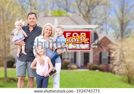 Happy Young Caucasian Family Outside In Front of Their New Home and Sold Real Estate Sign