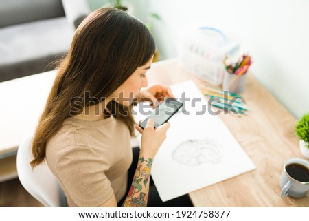 Top view of an attractive woman taking a photo of her drawing and posting it on social media. Latin woman with an art hobby sketching on a notebook