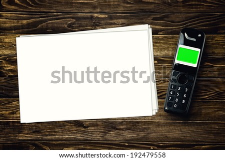 Wireless cordless phone and blank paper with copy space on wooden tabletop.