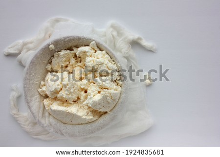 Close-up of freshly made white soft cottage cheese in bowl on white table background. Homemade ricotta in cheesecloth. Top view. Selective focus Royalty-Free Stock Photo #1924835681