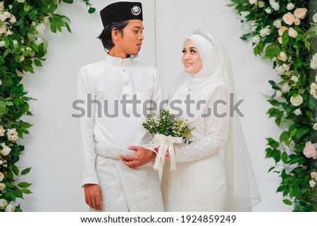 Happy beautiful bride and groom wearing white Malay traditional cloth pose during wedding celebration in Malaysia