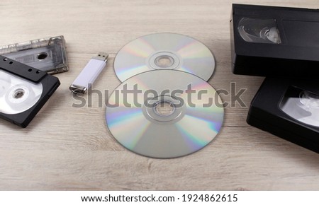 Various storage media. Discs, flash drive and old audio and video tapes on wooden background