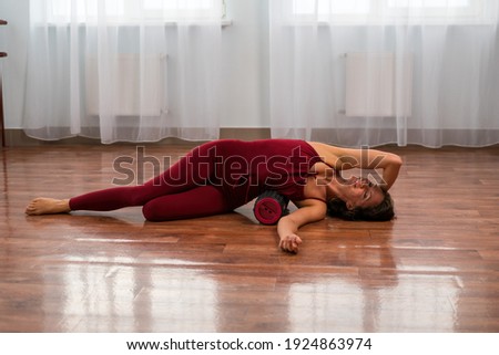 A young woman fitness instructor in red Sportswear Leggings and Top stretching in the gym before her pilates, on a yoga mat near the large window on a sunny day, female fitness yoga routine concept.