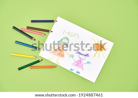Happy mothers day. Top view of a child drawing and colored pencils on a green background, handmade greeting card for the best mom in the word. Spring holidays and womens day celebration