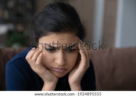 Close up of pensive sad young Indian woman look in distance think ponder of life problem solution. Unhappy thoughtful millennial mixed race female feel distressed depressed. Loner, outcast concept. Royalty-Free Stock Photo #1924895555