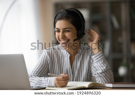 Overjoyed millennial Indian female student in headphones look at laptop screen study online from home. Happy young mixed race woman in earphones talk on video call with teacher. Virtual event concept. Royalty-Free Stock Photo #1924896320