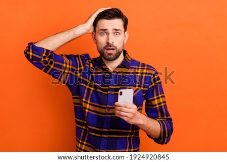 Photo of young man unhappy upset hand touch head use cellphone worried mistake fail problem isolated over orange color background