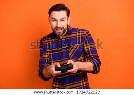 Portrait of excited young man playing games look interested camera wear checkered isolated on orange color background