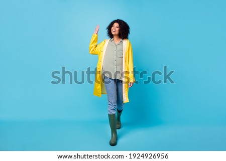 Photo of adorable charming dark skin lady wear yellow overcoat walking waving arm isolated blue color background