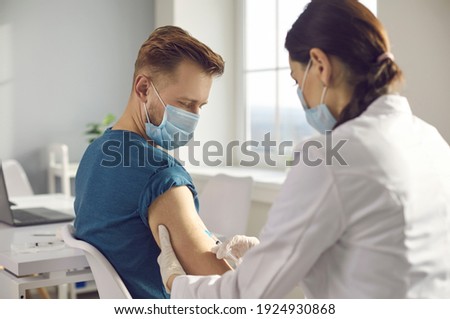 Man in medical face mask getting injection at hospital. Doctor or nurse holding syringe and giving shot to male patient. Global pandemic. New Covid-19 vaccine clinical trial. Immunization campaign Royalty-Free Stock Photo #1924930868