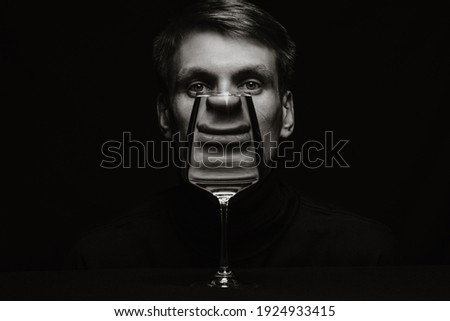 black and white unusual portrait of a man looking through a glass of water on a dark background