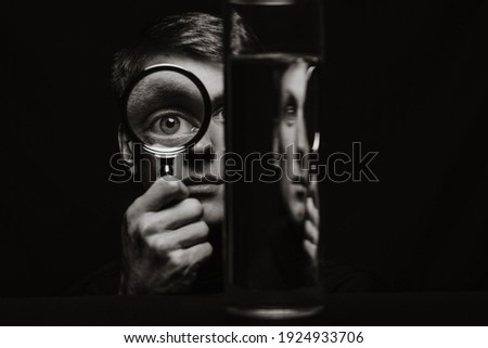 black and white portrait of a strange man looking through a magnifying glass and a container of water
