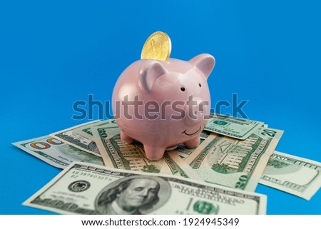 piggy bank with bit coin on background of US dollars banknotes on blue background