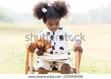 Cute African American toddler little girl learning, writing book while sitting on stepladder in the park. Black people little girl with curly hair learning outdoor