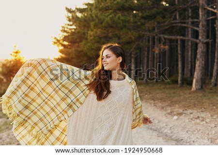 Happy woman in a checkered plaid and in a knitted dress walks near the coniferous trees