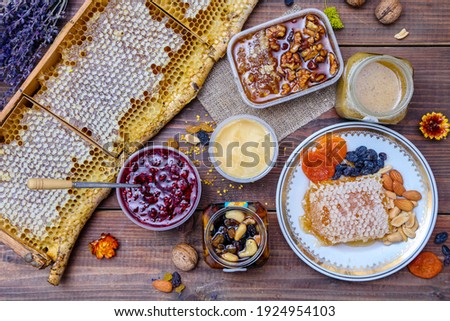 Rustic still life with honeycombs, different types of honey desserts: honey with dried fruits, jam with honey, honey souffle, dried fruits and nuts on a wooden background, top view