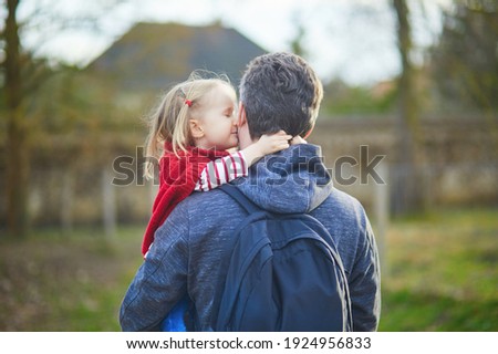 Man holding adorable toddler girl in his arms during a walk. Happy smiling daughter hugging and kissing her father. Fatherhood or father's day concept
