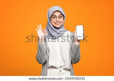Portrait of excited beautiful Asian woman showing okay sign and holding smartphone
