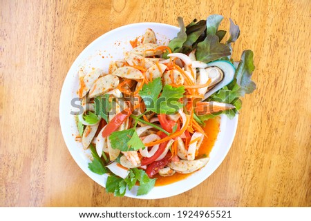 Thai spicy and tasty seafood and sausage salad in white dish on wooden table. 