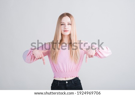 Portrait of a blonde girl who points her fingers down in the studio on a white background