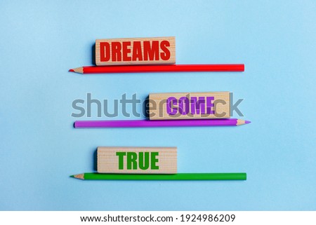 On a blue background, three colored pencils, three wooden blocks with text DREAMS COME TRUE