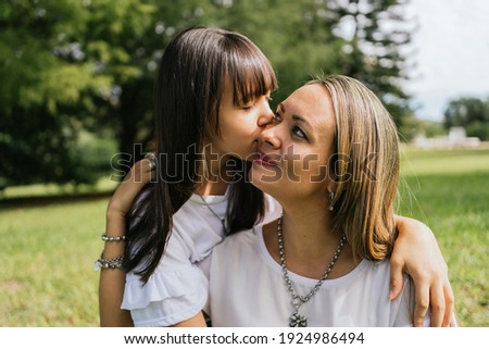 Teenage daughter kissing her mother outdoors.