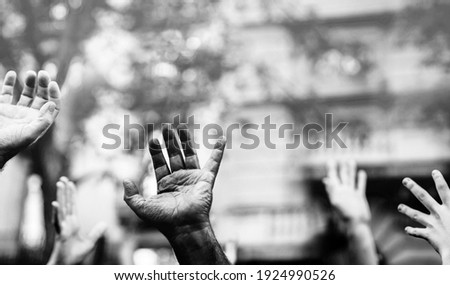 Open palm of a black hand and white hands raised in the air asking for freedom. Multicultural hands in a demonstration on street in black and white. Stop racism. Stop repression.