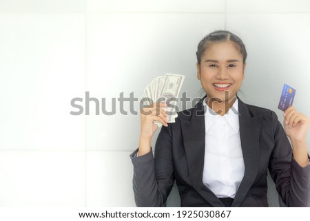 Portrait of young asian woman holding money and credit card looking at camera smiling. Copy space.