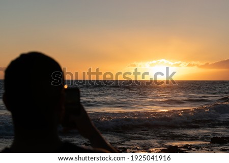 silhouette of young man on the beach taking pictures at sunset